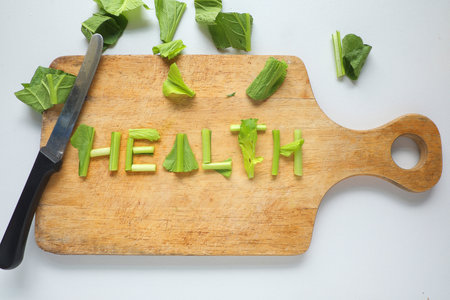 Health word made of pieces of green vegetable, that place on wooden cutting board with knife.の写真素材
