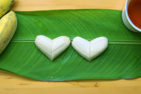 Banana pieces are arranged to two heart shape, place on fresh green leaf and wooden background.の写真素材