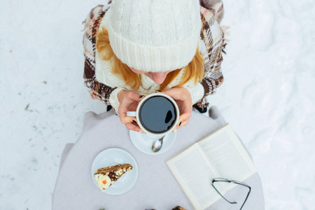 Woman holding cup of hot coffee on rustic wooden table, closeup photo  hands in warm sweater with mug, winter morning concept, top viewの写真素材