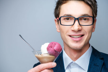Handsome young man with glasses, a blue jacket and white shirt with ice cream in a transparent glass in the studioの写真素材