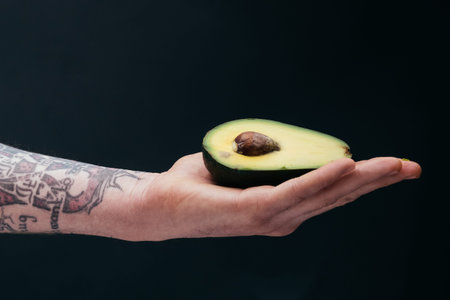 fresh avocado Tattooed mans hands Close-up on a dark background