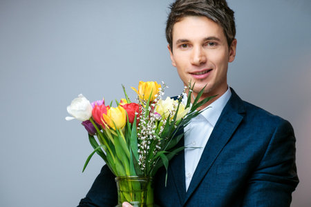 Young guy in a business suit in a studio with a bouquet of tulips. Flowers.の写真素材
