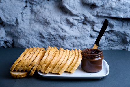 Sweet chocolate cream in jar on table. Nutella with buttered bread.の写真素材
