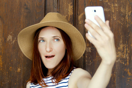 Girl making selfie outdoors. Portrait of a girl with red hair with a white phoneの写真素材