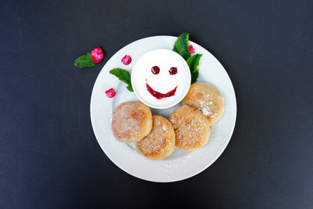 Pancakes on a plate with sour cream on a black background. Cheerful breakfast with a smile.の写真素材