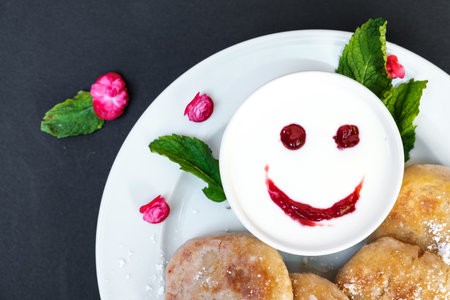 Pancakes on a plate with sour cream on a black background. Cheerful breakfast with a smile.の写真素材