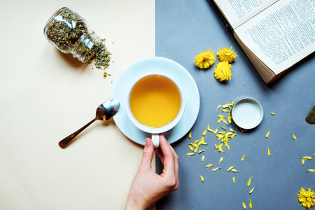 Cup and glass teapot with spicy hot fruit tea with orange and manggo next to an open book on table in cafeの写真素材