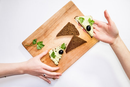 Top view of a woman holding a fresh avocado and making sandwiches on a table with other ingredients. Healthy life, diet, raw food,の写真素材