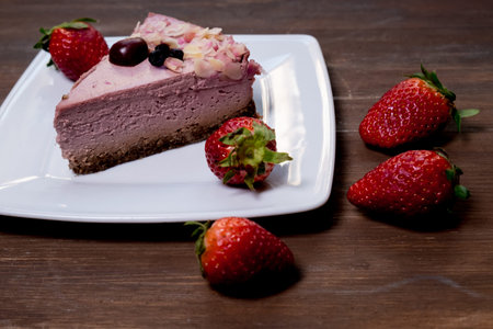 Strawberry cheesecake on black plate over rustic wooden background. Top view