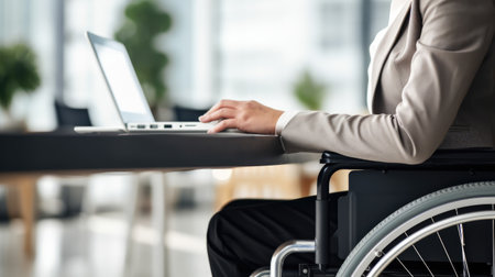 strength of diversity with a woman in a wheelchair at an office desk. Unrecognizable hand close-up. Ideal for promoting workplace equality and accessibility.の素材