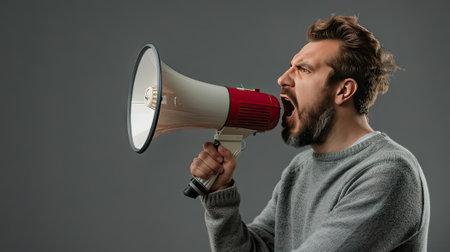 Man does announcement using a megaphone on a gray background, symbolizing effective communication and powerful announcementsの素材