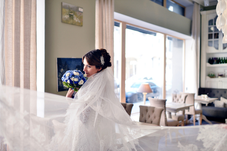 Beauty bride in bridal gown with bouquet and lace veil indoors.の写真素材