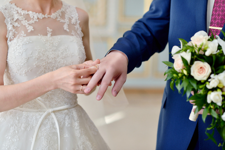 Beauty bride and handsome groom are wearing rings each other. Wedding couple on the marriage ceremony. Beautiful model girl in white dress. Man in suit. Female and male portrait. Cute lady and guyの写真素材