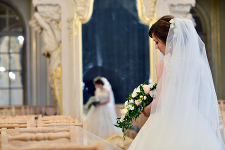 Beauty bride in bridal gown with bouquet and lace veil indoors. Beautiful model girl in a white wedding dress. Female portrait of cute lady. Woman with hairstyleの写真素材