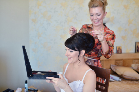 Wedding makeup artist making a make up for bride. Beautiful sexy model girl indoors. Beauty woman with curly hair. Female portrait. Bridal morning of a cute lady. Close-up hands near faceの写真素材