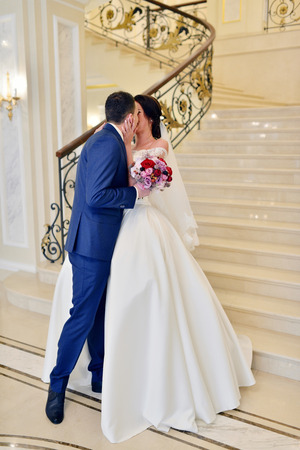 Handsome groom is seeing first the beauty bride in the morning. Meeting of a wedding couple. Beautiful model girl in white dress and in lace veil. Man in suit. Female and male portrait. Woman and guyの写真素材