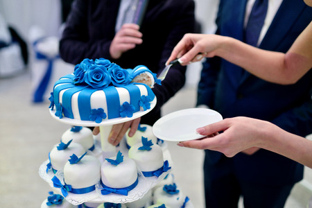 Beauty bride and handsome groom are cutting a wedding cake. Couple in the restaurant with colorful pie. Beautiful model girl in white dress. Man in suit. Female and male portrait. Cute lady and guyの写真素材