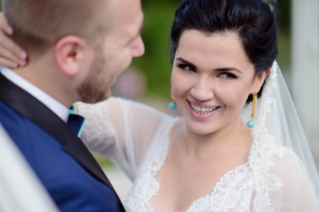 Wedding couple on the nature is hugging each other. Beautiful model girl in white dress. Man in suit. Beauty bride with groom. Female and male portrait. Woman with lace veil. Lady and guy outdoorsの写真素材