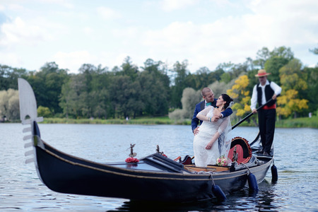 Wedding couple is hugging on a floating gondola. Beauty bride with groom. Beautiful model girl in white dress. Man in suit. Female and male portrait. Woman with lace veil. Cute lady and guy outdoorsの写真素材