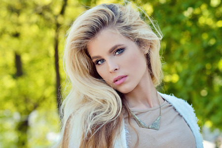 Fashionable portrait of lady with long hair in city. Image of blonde model on bright background. Young beautiful human in park. Adult female person outdoorsの写真素材