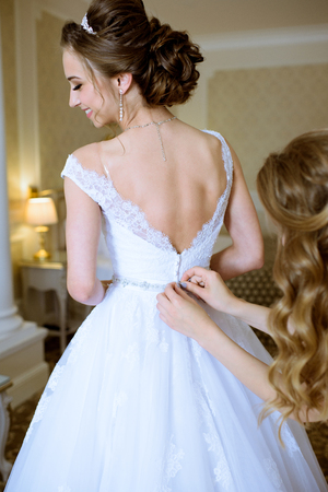 Bridesmaid is lacing white wedding dress for beautiful brideの写真素材