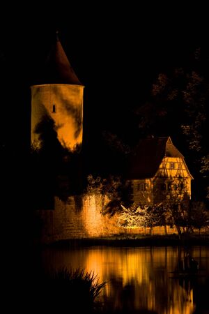 Medieval house and tower near water at night timeの写真素材