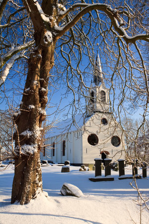Tree and church in a cold white winter landscapeの写真素材