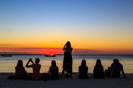 Women sitting on the beach watching the sunset overl the oceanの写真素材