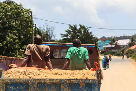 Men sitting in the back of a truck loaded with sand in Africaの写真素材