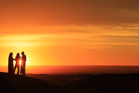 silhouette of three men standing in the desert at sunsetの写真素材