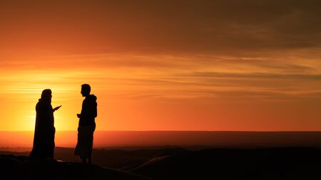 silhouette of three men standing in the desert at sunsetの写真素材