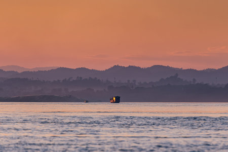Fishing boat in the sea at sunset with mountains in the backgroundの写真素材