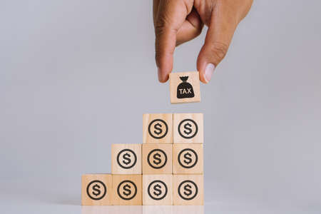 Tax Concept with wooden block.Man hand picking up wooden block with money icon and block of tax icon standing out from other.の写真素材