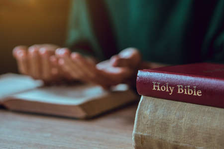Hands of man with Bible praying.Christian life prayer to god. Man Pray for god.believe in goodness. Holding hands in prayer on a wooden table.の写真素材