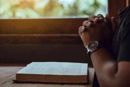 Hands of man with Bible praying.Christian life prayer to god. Man Pray for god.believe in goodness. Holding hands in prayer on a wooden table.の写真素材