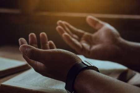 Hands of man with Bible praying.Christian life prayer to god. Man Pray for god.believe in goodness. Holding hands in prayer on a wooden table.の写真素材