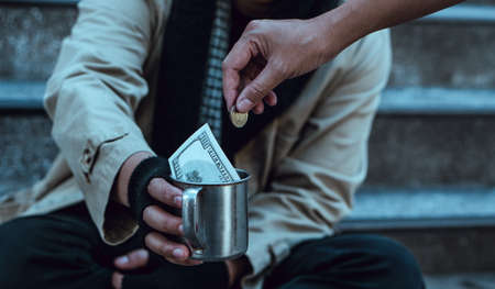 Woman giving money to homeless beggar man sitting in city.Giving concept.の写真素材
