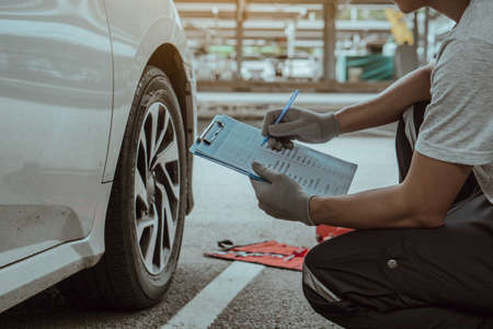 Mechanic holding the clipboard to checking car wheel in auto service garage.Repair or maintenance auto service.の写真素材