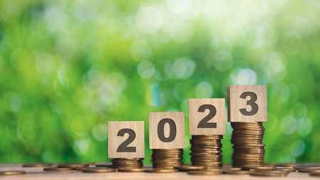 Close up stack of coin and 2023 wooden text block with green backgound on wood table.saving and...