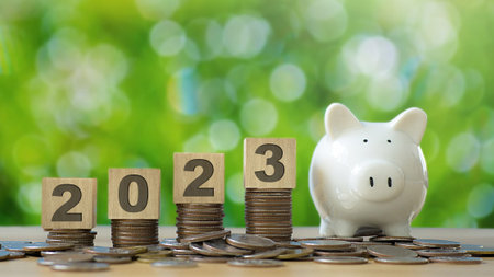 2023 wooden text block on stack of coin and piggy bank with green backgound.saving and manage money...
