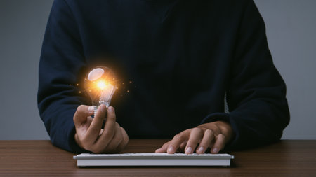 Creative thinking idea for Tecnology concept.Hand of young man holding light bulb with orange glowing and keyboard.Creative thinking idea concept.の写真素材