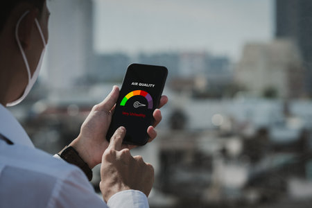 Man scanning the weather on his phone.Unhealthy weather.Allergies.health care.Young man wearing protection mask over smog city building with bad weather, pm2.5,City air pollution concept.の写真素材