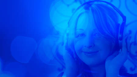 Young pretty woman listening music blue light backgroundの写真素材
