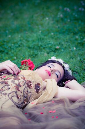 SLEEPING BEAUTY lying on the forrest with a roseの写真素材