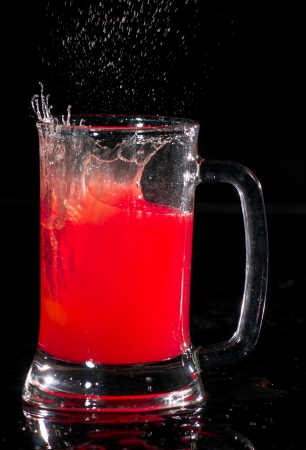 Red drink with a splash on a beer glass の写真素材