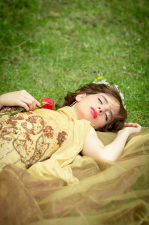 Sleeping beauty lying on the grass in the forest with a roseの写真素材