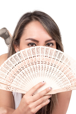 young latin woman holding a fan in front of her face isolated over whiteの写真素材
