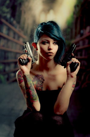 provocative tattooed girl in black dress poiting guns to the sidesの写真素材