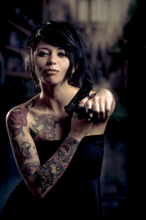 Beautiful tattooed girl in black dress with attitude pointing gun to cameraの写真素材