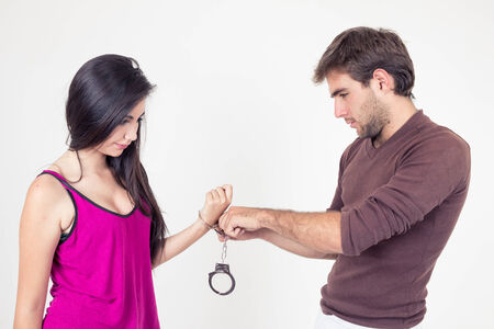 Handsome young man putting handcuffs on beautiful young girl isolated on whiteの写真素材